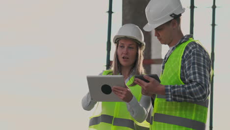 Building-in-construction-with-a-female-and-a-male-builders-constructors-engineers-walking-along-it